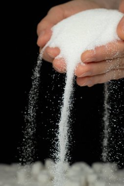 Hands pouring white crystalline refined sugar, black background. clipart