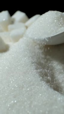 Beyaz kristal şeker kaşıkta, dikey ağır çekimde.