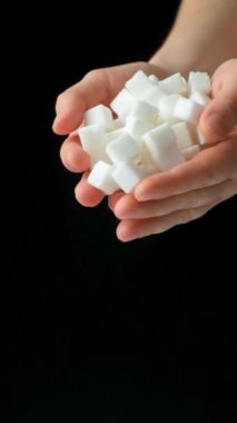 Eller beyaz baskılı pancar kökü küplerini döküyor rafine şeker, siyah arkaplan, dikey ağır çekim