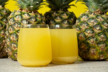 Pineapple juice in glasses among fresh pineapples clipart