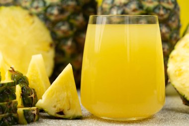 Ananas suyu bardakta, taze ananas meyvesinin yanında.