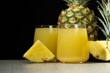 Ananas suyu bardakta, taze ananas meyvesinin yanında.
