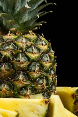 Whole pineapple and cut into pieces on a black background close-up clipart