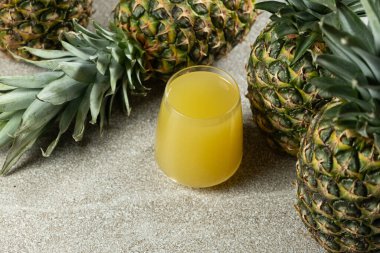 Ananas suyu bardakta, taze ananas meyvesinin yanında.