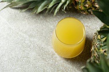 Ananas suyu bardakta, taze ananas meyvesinin yanında.