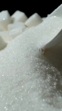 Beyaz kristal şeker kaşıkta, dikey ağır çekimde.
