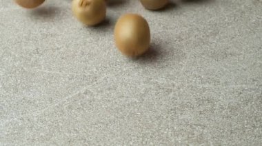 Birçok taze, soyulmamış kivi meyvesi ağır çekimde gri bir arka planda yuvarlanıyor..