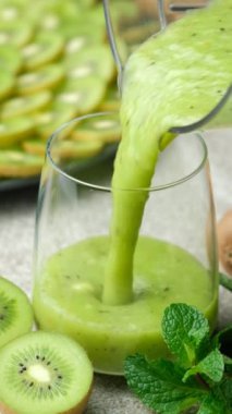 Taze yeşil kivili smoothie blender kasesinden cama dökülüyor. Dikey ağır çekim.