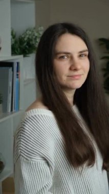 30 yaşında, makyajsız, uzun saçlı esmer bir kadın kameraya bakıyor ve gülümsüyor.