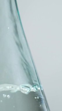 Beyaz damıtılmış sirke cam kaseye dökülüyor, dikey makro ağır çekimde. Temiz sıvıda kabarcıklar.