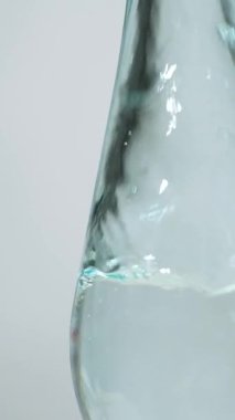 Beyaz damıtılmış sirke cam kaseye dökülüyor, dikey makro ağır çekimde. Temiz sıvıda kabarcıklar.