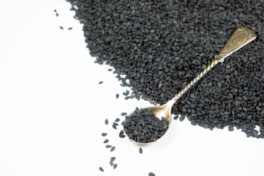 Beyaz arka planda kaşıkta siyah susam tohumları.
