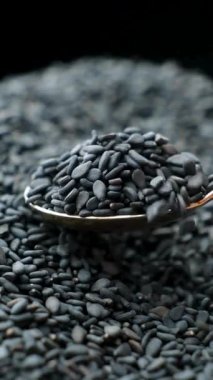 Çiğ siyah susam tohumları kaşıkta, dikey ağır çekimde..