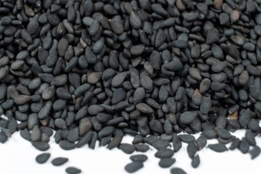 Soyulmamış siyah susam tohumları beyaz arka plan makro fotoğrafçılığına saçılmış.