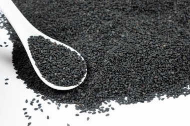 Beyaz arka planda kaşıkta siyah susam tohumları.