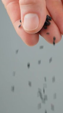 El, siyah susam dökerken yavaş çekim dikey