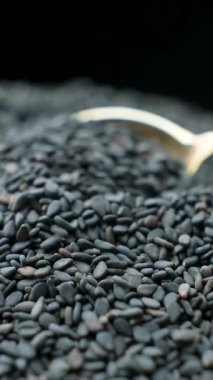 Çiğ siyah susam tohumları kaşıkta, dikey ağır çekimde..