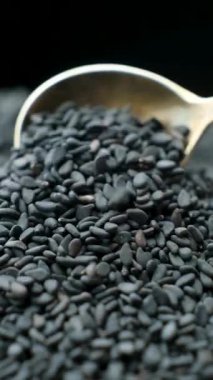 Çiğ siyah susam tohumları kaşıkta, dikey ağır çekimde..