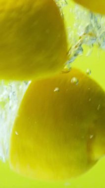 Taze limonların yarısı suya batırılır, kabarcıklar oluşur, dikey ağır çekimde..