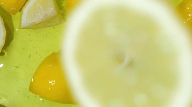 Limon dilimi suya düşüyor yavaş çekimde yukarı doğru sıçrıyor. Meyve arkaplanı tazeleniyor.