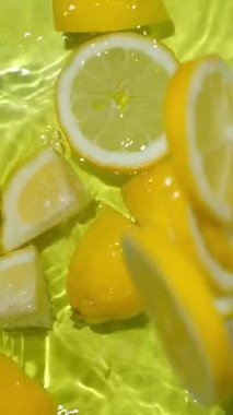 Limon dilimi suya düşüyor yavaş çekimde yukarı doğru sıçrıyor. Dikey meyve arkaplanı.