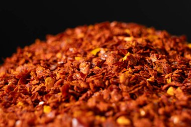 Kurumuş ve öğütülmüş kırmızı biber yığını siyah arkaplanda yoğun baharat bırakıyor..