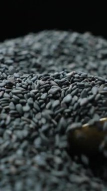 Çiğ siyah susam tohumları kaşıkta, dikey ağır çekimde..