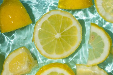 Turkuaz narenciye arkaplanı yüzen sarı limon parçalarıyla tazeleniyor.