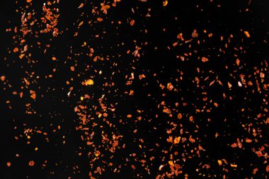 Ezilmiş kırmızı biber, baharatlı baharat, siyah arkaplandan dökülüyor..