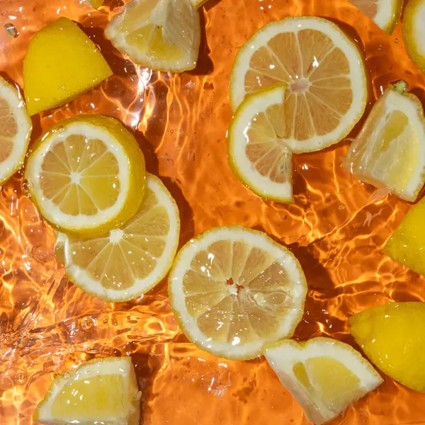 Suda taze limon dilimleri, biraz su, taze turuncu arka plan, üst manzara..