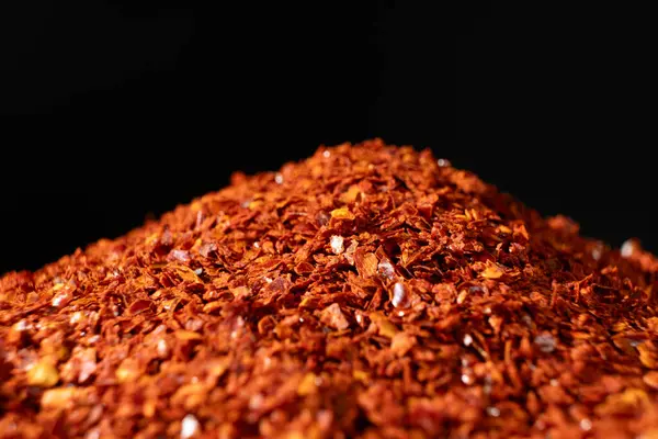 Kurumuş ve öğütülmüş kırmızı biber yığını siyah arkaplanda yoğun baharat bırakıyor..