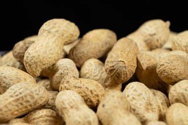 Kabuk içinde soyulmamış fıstık yığını. Siyah arka planda yakın plan.