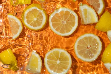 Suda taze limon dilimleri, biraz su, taze turuncu arka plan, üst manzara..