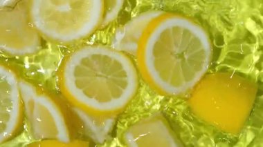 Limon dilimi suya düşüyor yavaş çekimde yukarı doğru sıçrıyor. Meyve arkaplanı tazeleniyor.