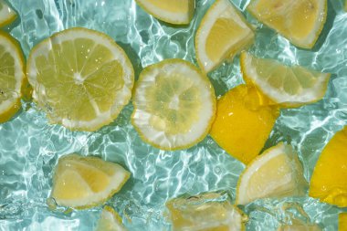 Turkuaz narenciye arkaplanı yüzen sarı limon parçalarıyla tazeleniyor.