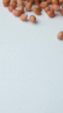 Kurumuş fıstık çekirdeklerini beyaz arka planda, dikey yavaş çekimde serpiştiriyorlar..