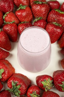 Taze çileklerin arasında bir bardakta çilekli tatlı milkshake.