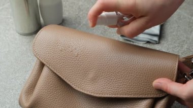 Deri bir el çantasının yüzeyini temizliyorum. Püskürtme uygulaması ve bez ile silme, yavaş çekim.