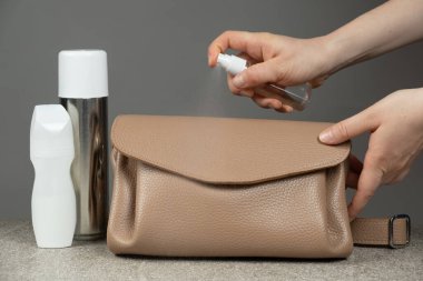 Deri ürünlerin bakımı. Ürünün özel bir spreyini deri bir el çantasının yüzeyine sürerek.