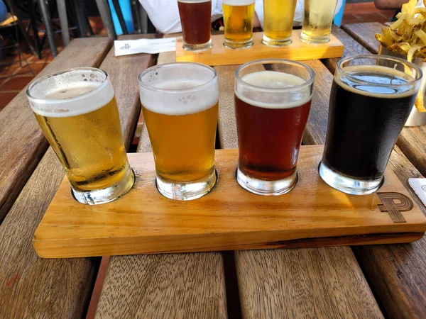 四个不同类型啤酒的采样器在木制底座和餐桌上的图像 — 图库照片