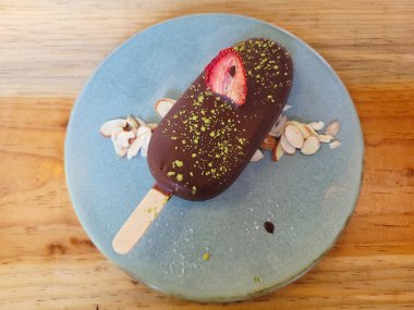 Lezzetli bir dondurma paletiyle anın tadını çıkarın. Yumuşak çikolatayla kaplanmış, ahşap bir masada zarif bir şekilde sunulmuş.