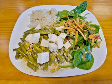 Baharatlı yeşil fasulye, kabarık beyaz pirinç ve beyaz peynirli taze ıspanak salatası içeren besleyici bir vejetaryen yemeği.