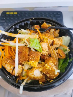 Sağlıklı çıtır tavuk salatası, siyah servis konteynırında servis ediliyor. Paramparça havuç ve peynir serpiştirilmiş.