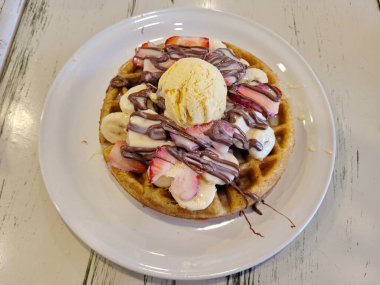 Vanilyalı dondurma, çilek ve çikolatayla kaplı taze pişmiş waffle 'ın üstünde.