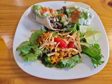 Taze soslu nefis bir biftek burrito ve yanında çıtır tortilla şeritleriyle süslenmiş bir salata.