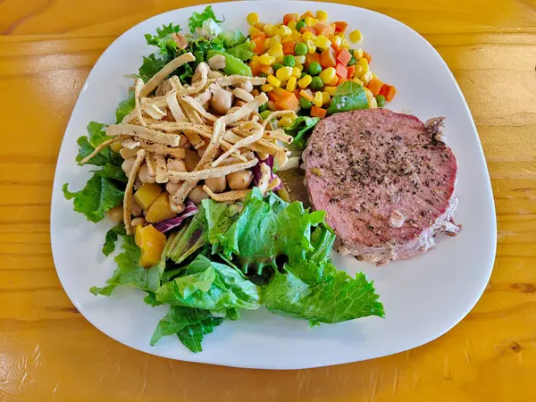 A beautifully plated seared tuna steak alongside a vibrant mixed salad and colorful corn salsa