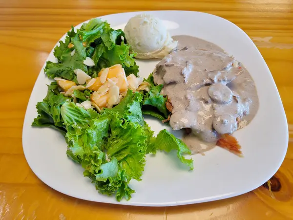 Grilled steak topped with a creamy mushroom sauce, served with a leafy green salad and almond slivers