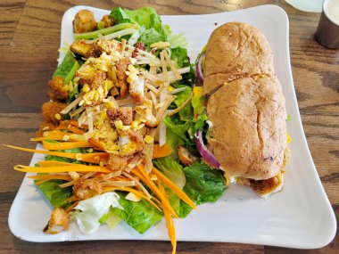 Zarif beyaz tabakta servis edilen sağlıklı bir sandviçin yanında çıtır tavuk salatası bulunan leziz bir karışım yemek.