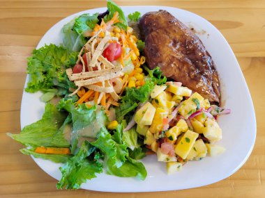 Lezzetli ızgara tavuk göğsü ve yanında canlı bir bahçe salatası ve beyaz tabakta ferahlatıcı bir mango sosu.