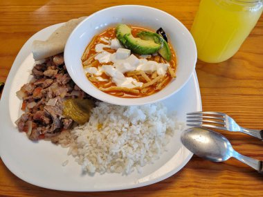 Avokado ve peynirle kaplı bir kase zengin çorbayla nefis Meksika yemeği, baharatlı et, beyaz pirinç ve yumuşak tortilla ile servis edilir.